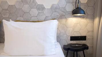Una cama con un almohadón blanco, una lámpara negra y un diseño de pared hexagonal.