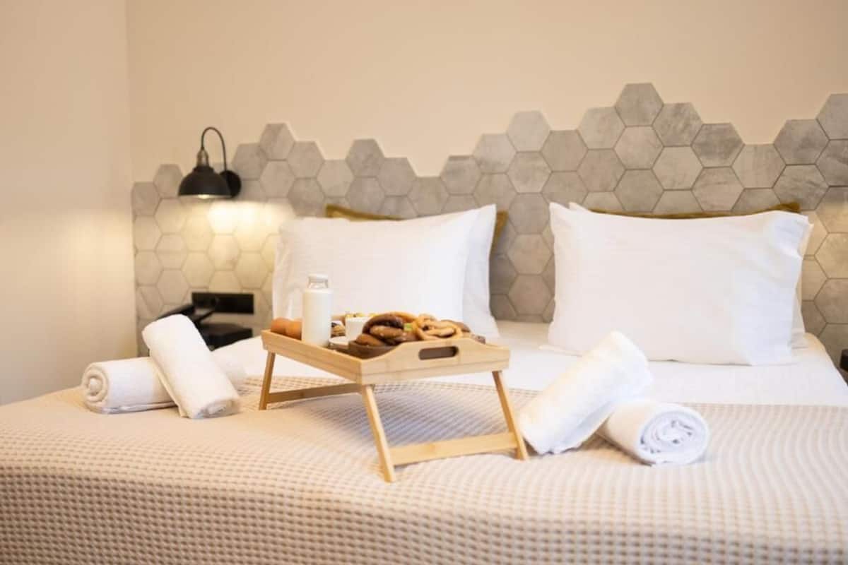 Une chambre d’hôtel avec un lit, un plateau contenant des articles pour le petit-déjeuner, une lampe et un motif hexagonal sur le mur.