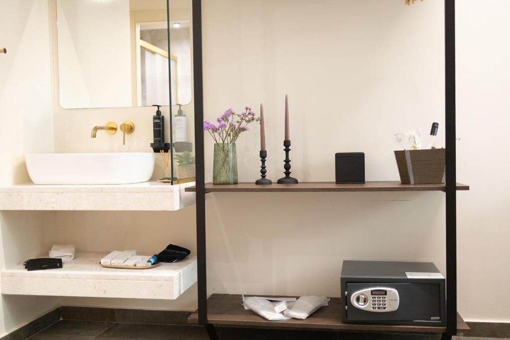A bathroom with a white sink, a mirror, a shelf with candles, a vase with flowers, a black safe, and a towel rack.