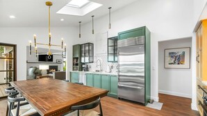 A modern kitchen with a large wooden dining table, stainless steel appliances, and a skylight. - Greenbank Horizon Home | Water Views (Greenbank)