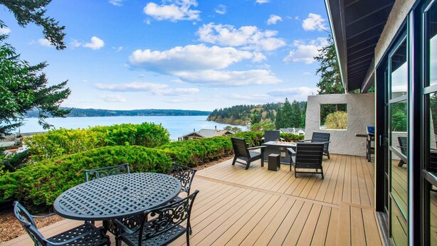A deck with a table and chairs, overlooking a lake and forested hills. - Greenbank Horizon Home | Water Views (Greenbank)