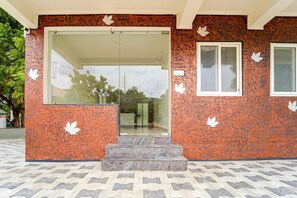 Una entrada de edificio con puerta de vidrio, una ventana pequeña y unos escalones que suben a la puerta.