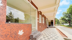 A building with a glass entrance, a red textured wall, and a tiled walkway leading to a door.