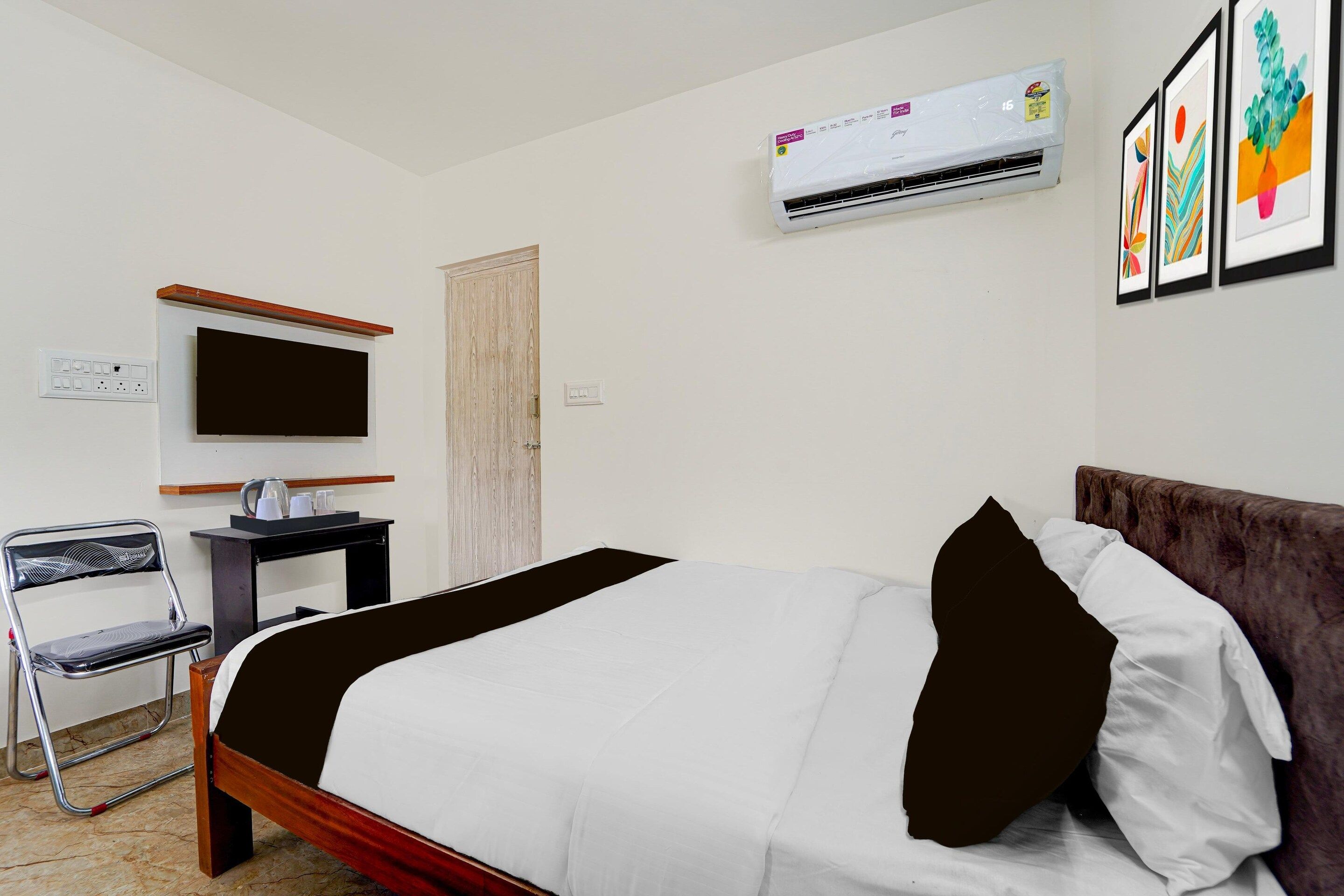 A hotel room with a bed, a desk, a chair, a television, an air conditioner, and a door.