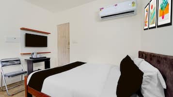 A hotel room with a bed, a desk, a chair, a television, an air conditioner, and a door.