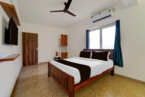 A bedroom with a bed, a ceiling fan, an air conditioning unit, a window with curtains, and a wooden door. - Townhouse MK University Bus Terminal Madurai (Madurai)