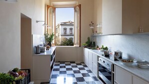 Een smalle keuken met een geruite vloer, een raam met een geopende deur, en uitzicht op gebouwen.