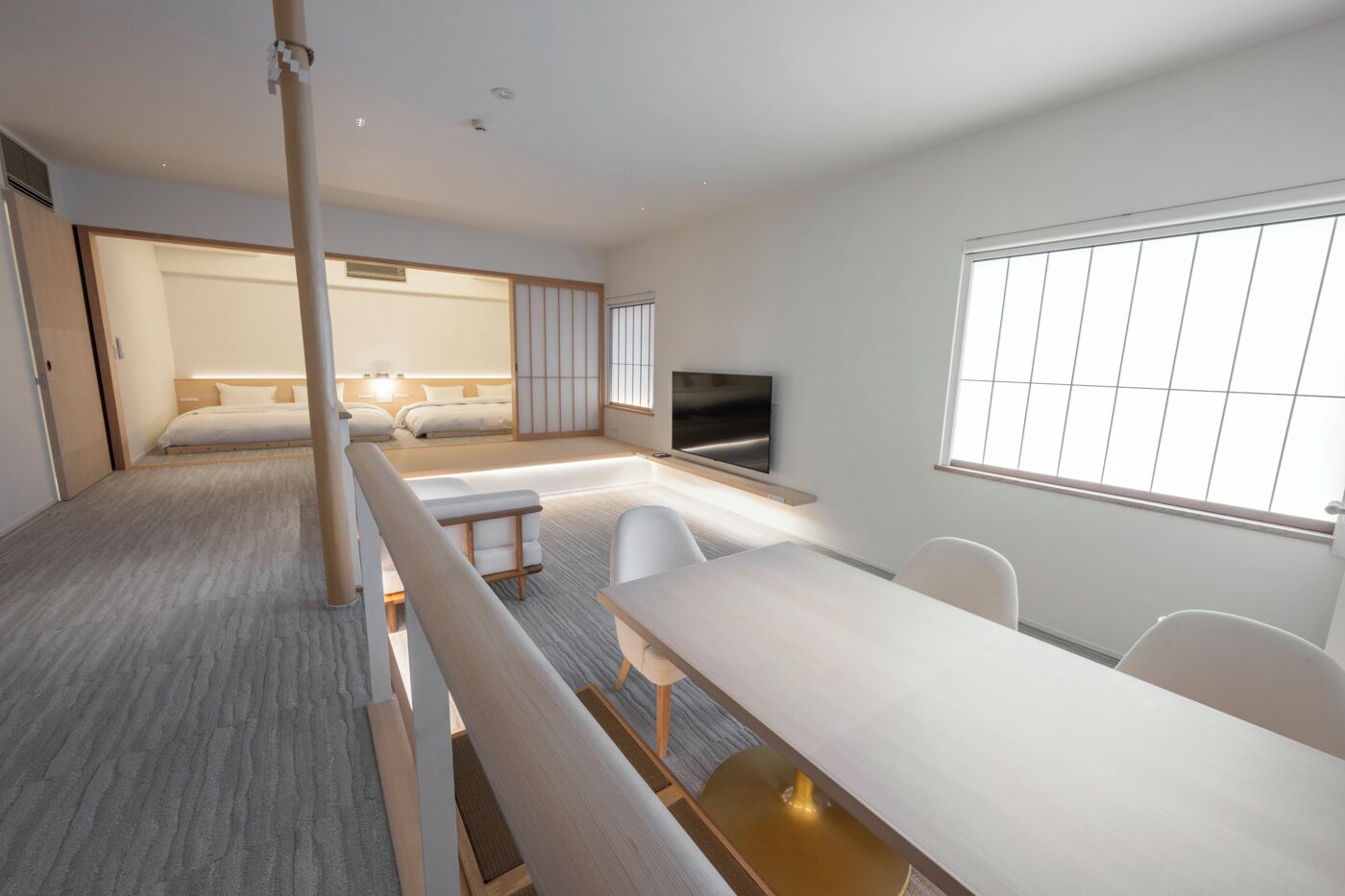 A modern hotel room with a bed, a TV, a dining area, and a large window.