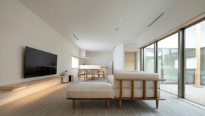 Una camera d'hotel moderna con una grande TV a schermo piatto, un divano, un'area pranzo e ampie finestre.