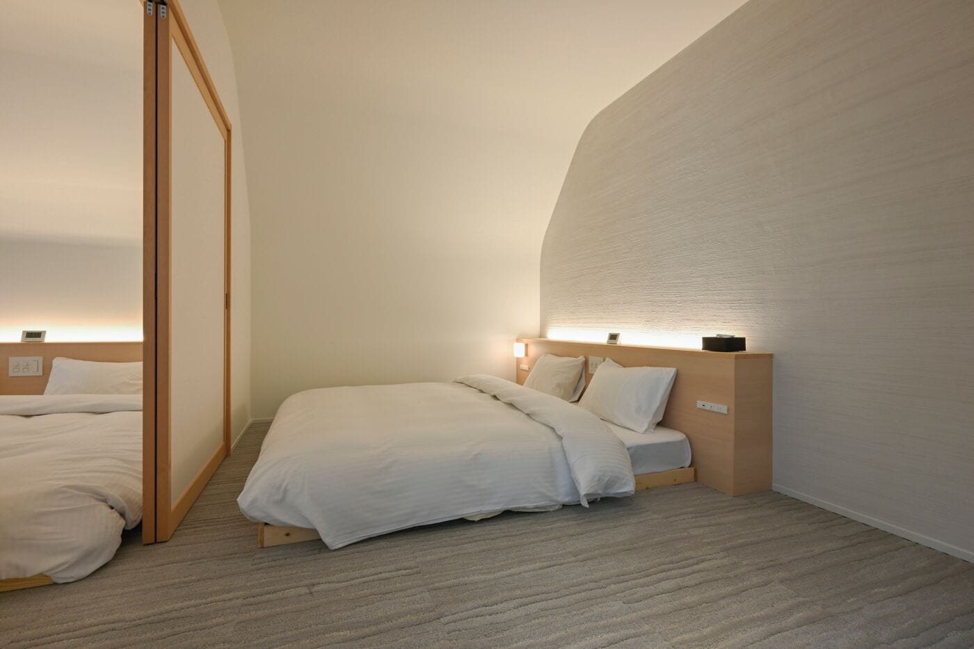 A hotel room with two beds, wooden headboards, and a large wall with a textured surface.