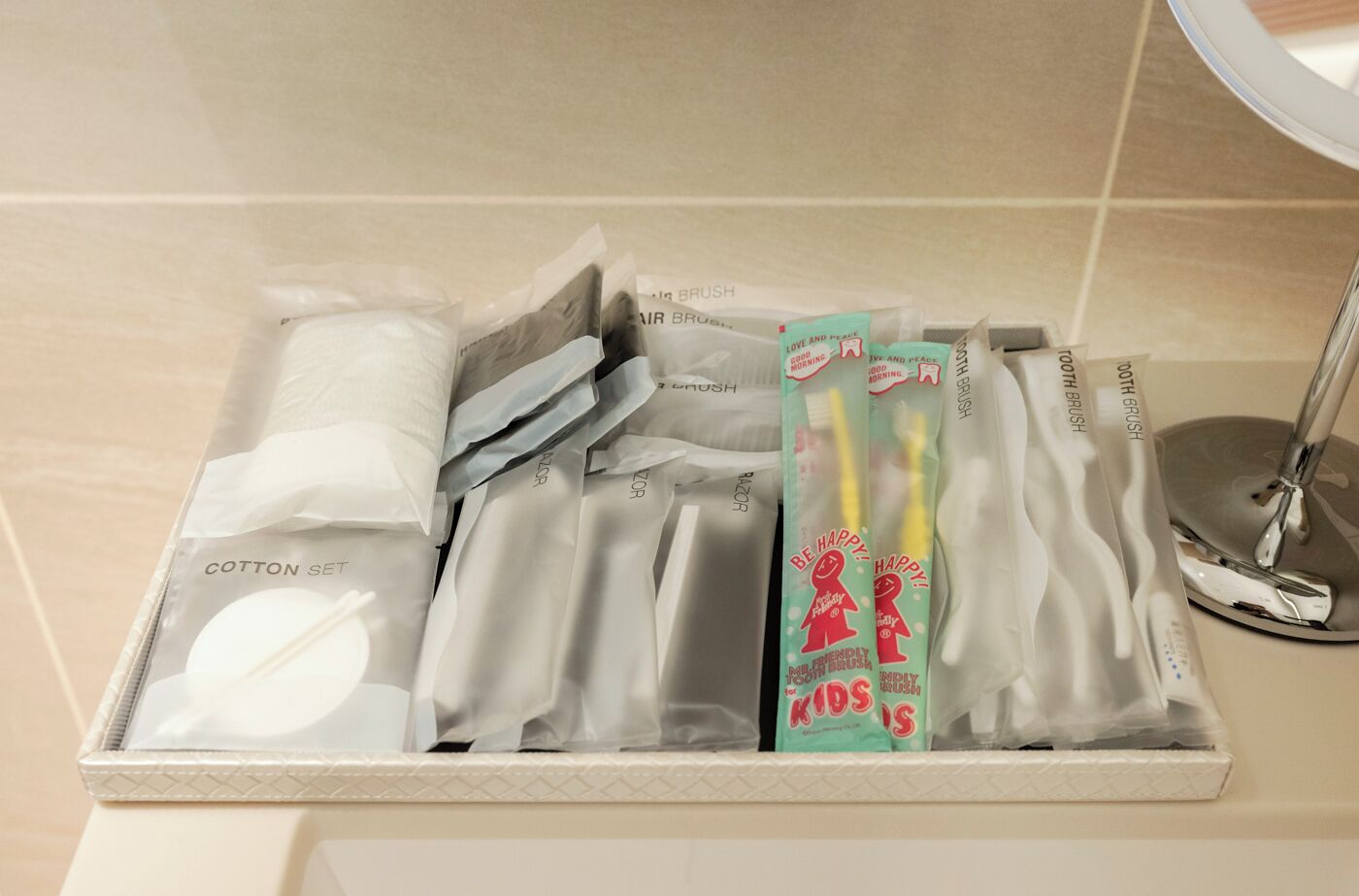 A bathroom with a tiled floor, a sink with a chrome faucet, and a storage box containing cotton pads, toothbrushes, and toothpaste.