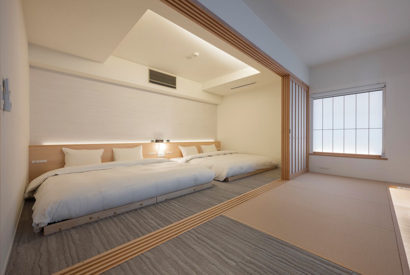 Una habitación de hotel moderna con dos camas, un tragaluz, un ventanal grande y un diseño minimalista.