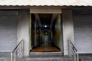 A corridor with a wooden floor leading to a closed door, metal railings, and a ceiling light. - Deluxe Hotel Koshalya Mohan (Jabalpur)