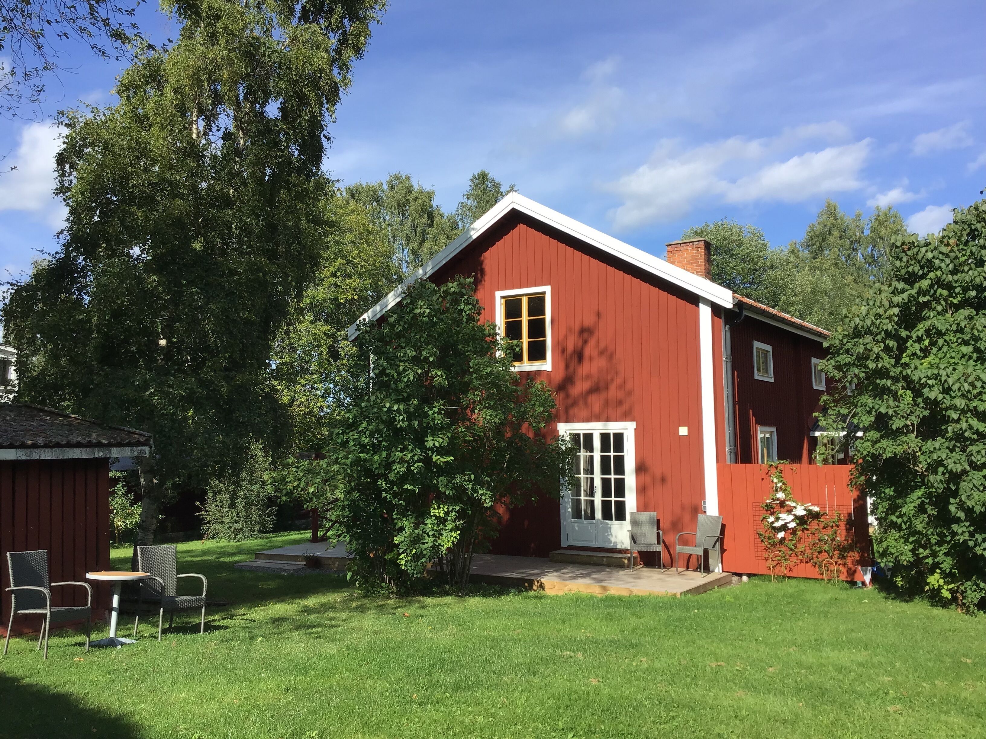 A red house with a white door, surrounded by green trees and a well-maintained lawn.
