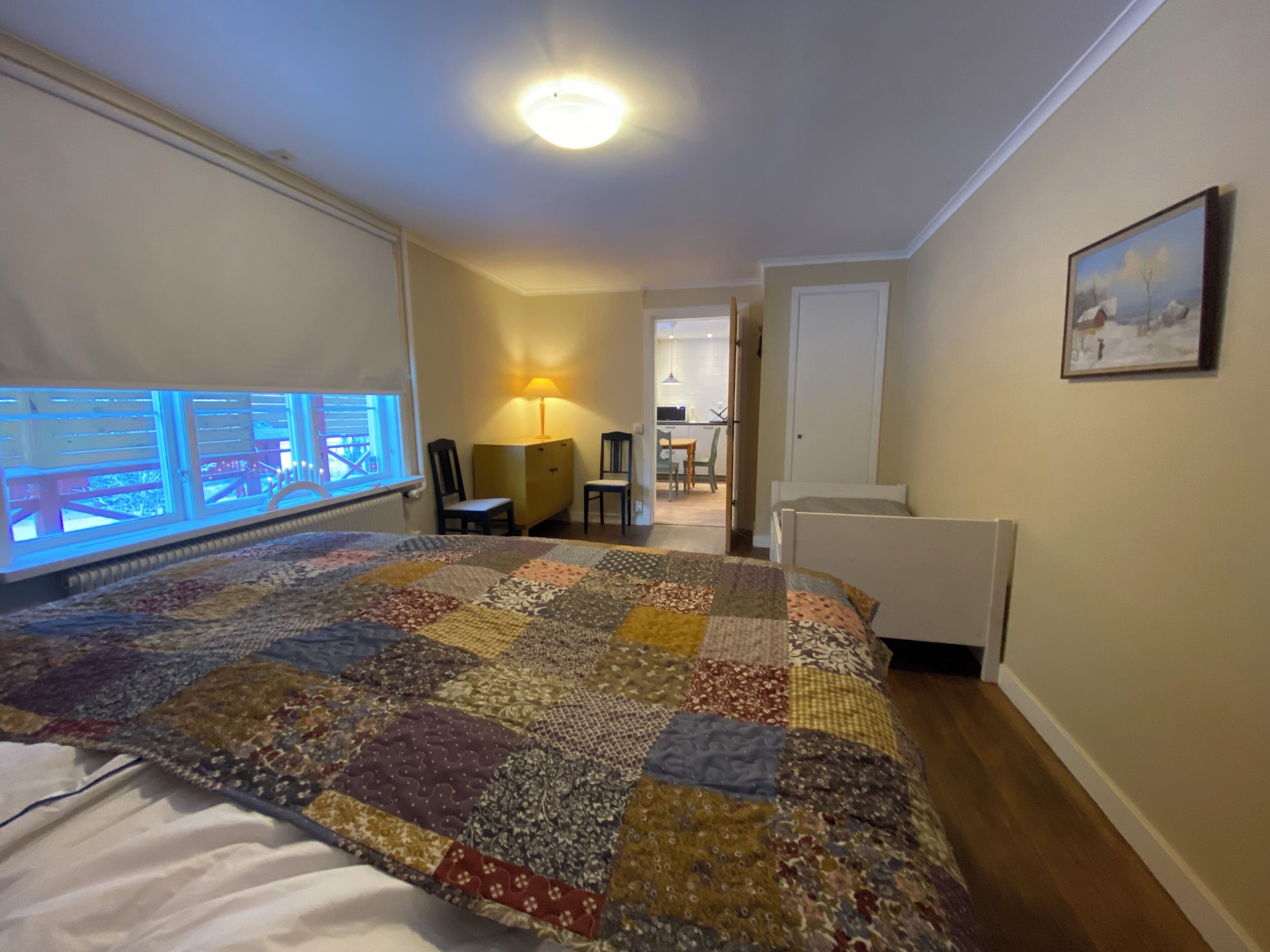 Ett sovrum med en stor säng, ett skrivbord, en stol, en lampa och utsikt över en balkong.