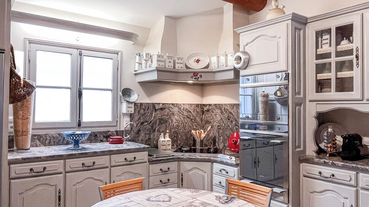 A kitchen with a marble backsplash, white cabinetry, and a dining area with a table and chairs.