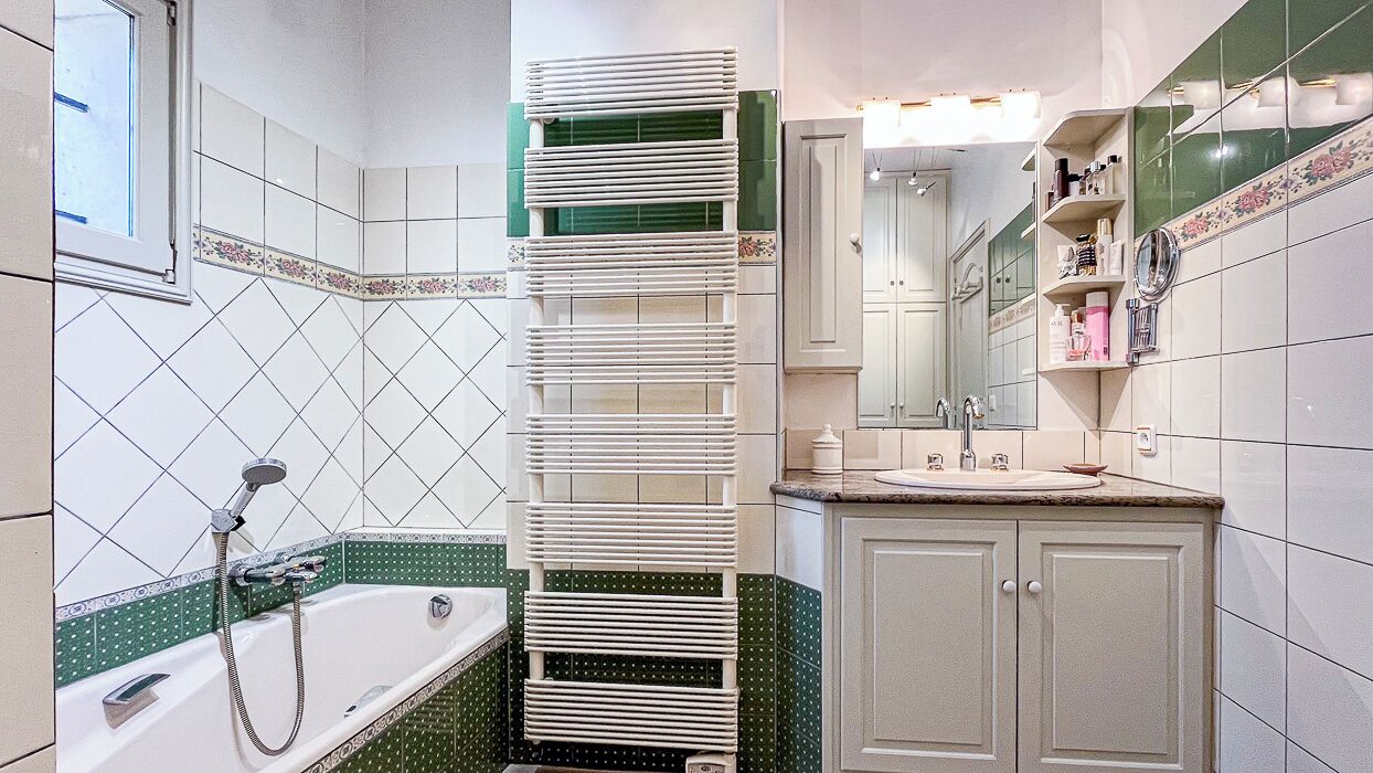 Une salle de bain équipée d’une baignoire, d’une douche, d’un lavabo et d’un miroir. On y trouve également des armoires et des étagères contenant des articles de toilette.