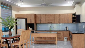 A modern kitchen with wooden cabinets, a dining area with a table and chairs, and a built-in oven. - An's Home Ninh Binh (Ninh Binh)