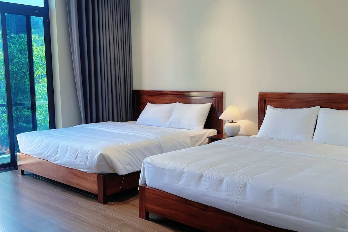 Habitación de hotel con dos camas de madera, un ventanal con cortinas y vistas a la vegetación.