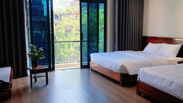 A hotel room with two beds, a small table with a plant, and a balcony with a view of greenery. - An's Home Ninh Binh (Ninh Binh)