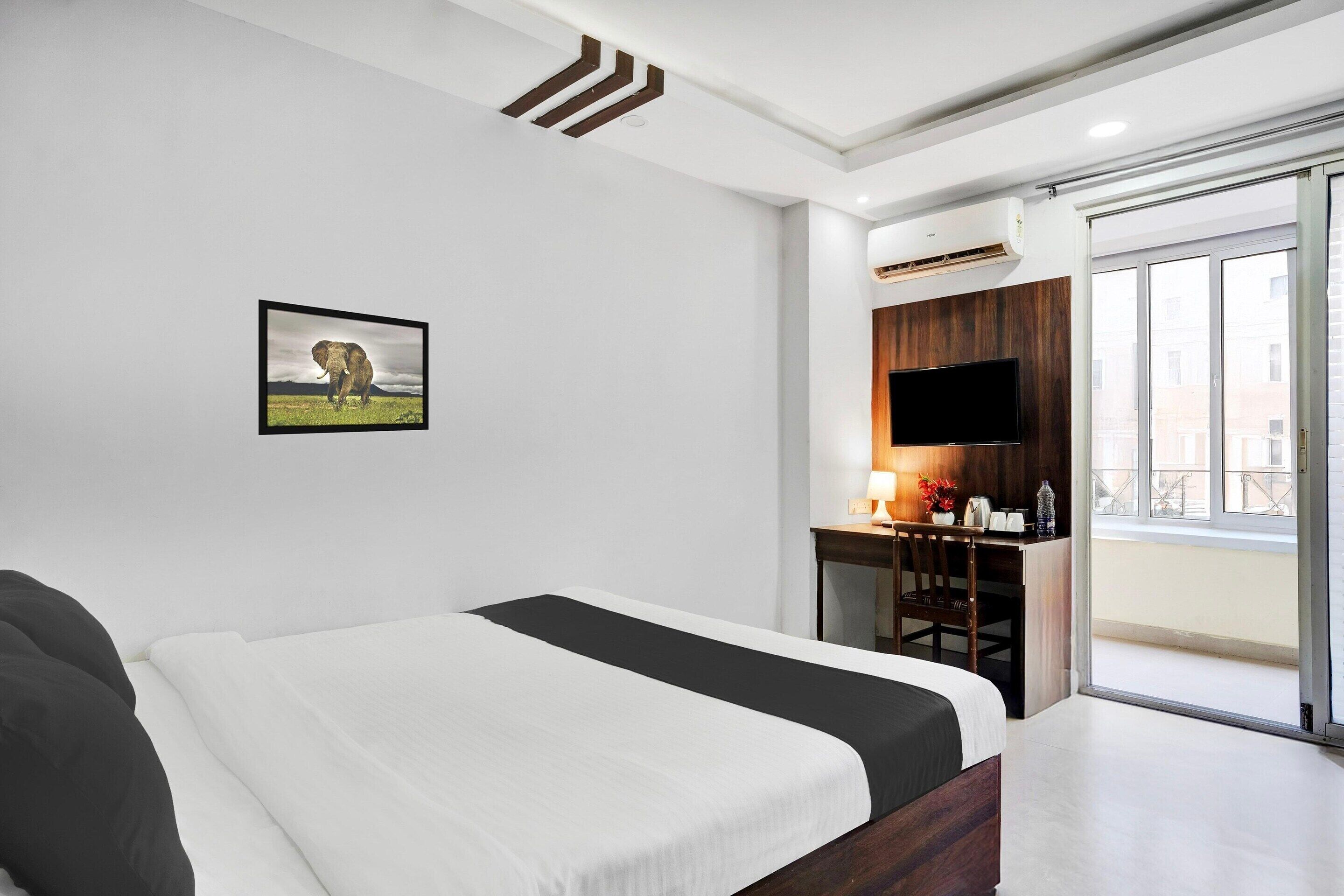 Una camera d'hotel con un letto, una scrivania con televisore, un quadro appeso e vista dalla finestra.