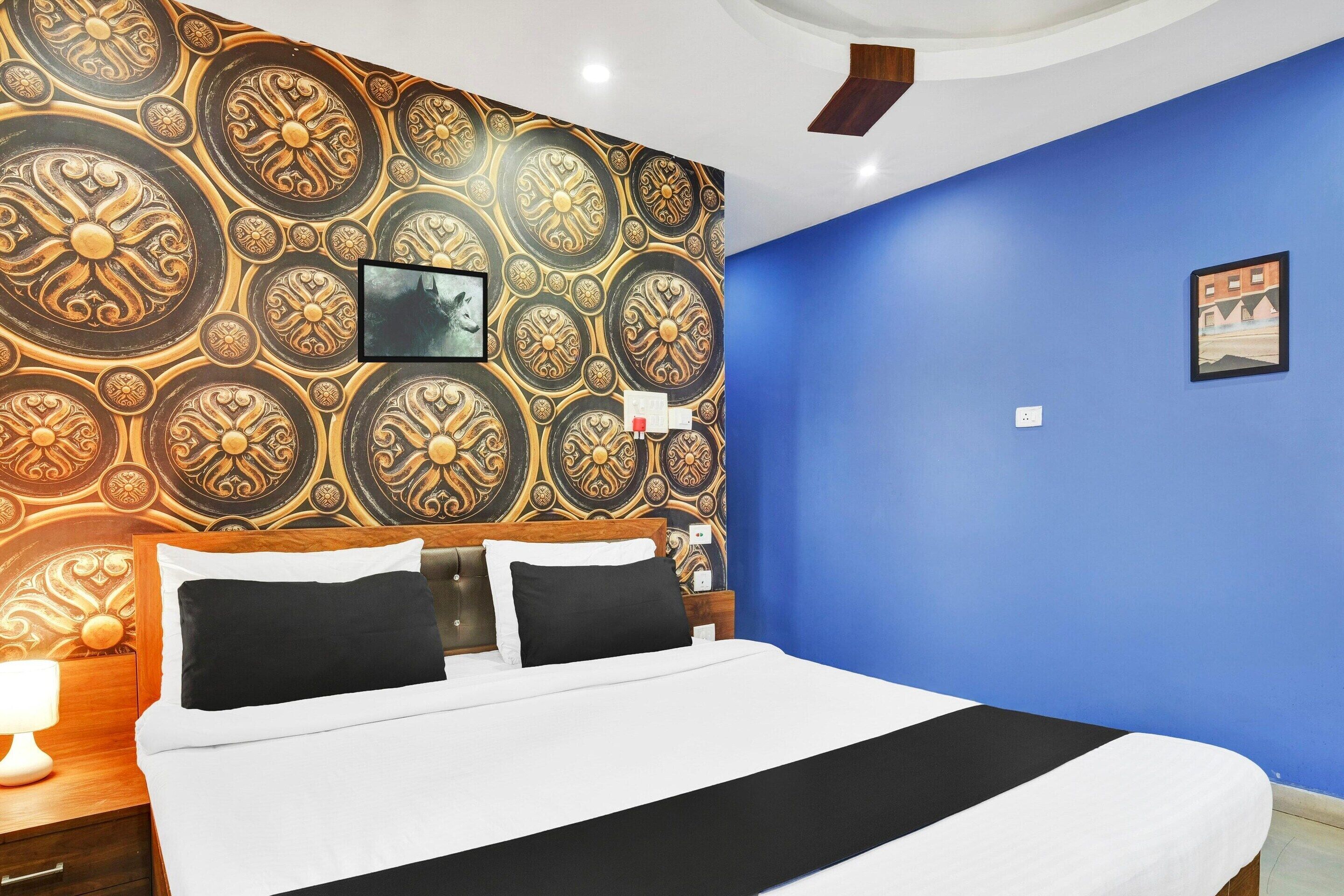 A hotel room with a large bed, a wooden headboard, a blue accent wall, and a decorative wall pattern.