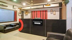 A reception area with a sign reading 'TOWNHOUSE Company Serviced,' a seating area with a large screen, and a ceiling fan. - Classic With Balcony Luxuria Ganeshguri (Guwahati)
