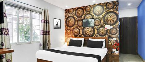 Un dormitorio con cama, televisor, pared decorativa, ventana con cortinas y puerta.