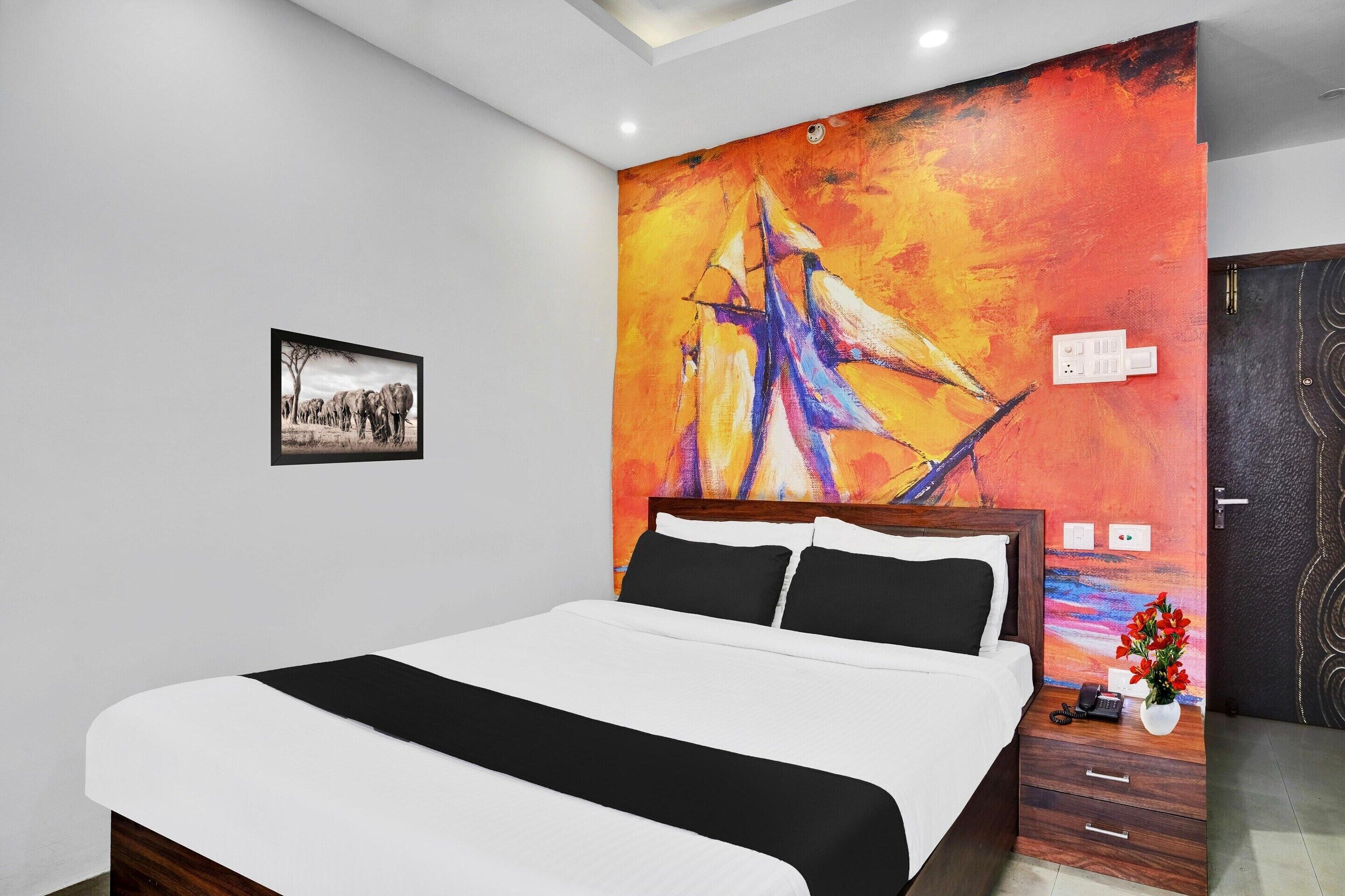 A hotel room with a large bed, a painting on the wall, a small table with a vase, and a door with a unique design.