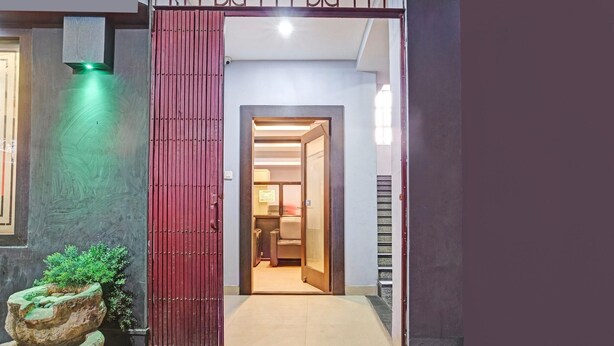 A modern entrance with a red door, a stone planter with greenery, and a well-lit interior visible through the doorway. - Classic With Balcony Luxuria Ganeshguri (Guwahati)