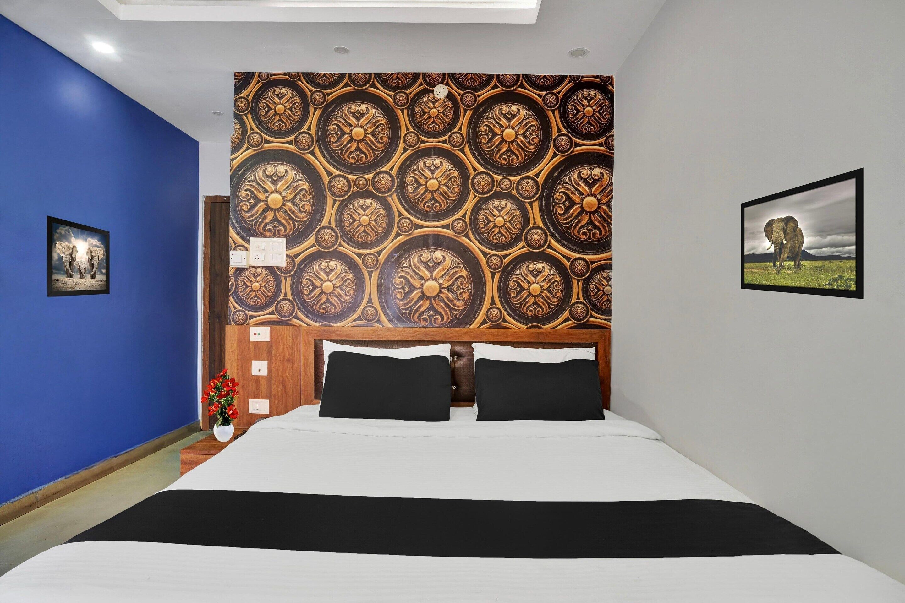 Ein Schlafzimmer mit einem gemusterten Kopfteil, einem Bett mit schwarz-weißer Bettwäsche, einem Nachttisch mit Blumen in einer Vase und einem gerahmten Bild an der Wand.