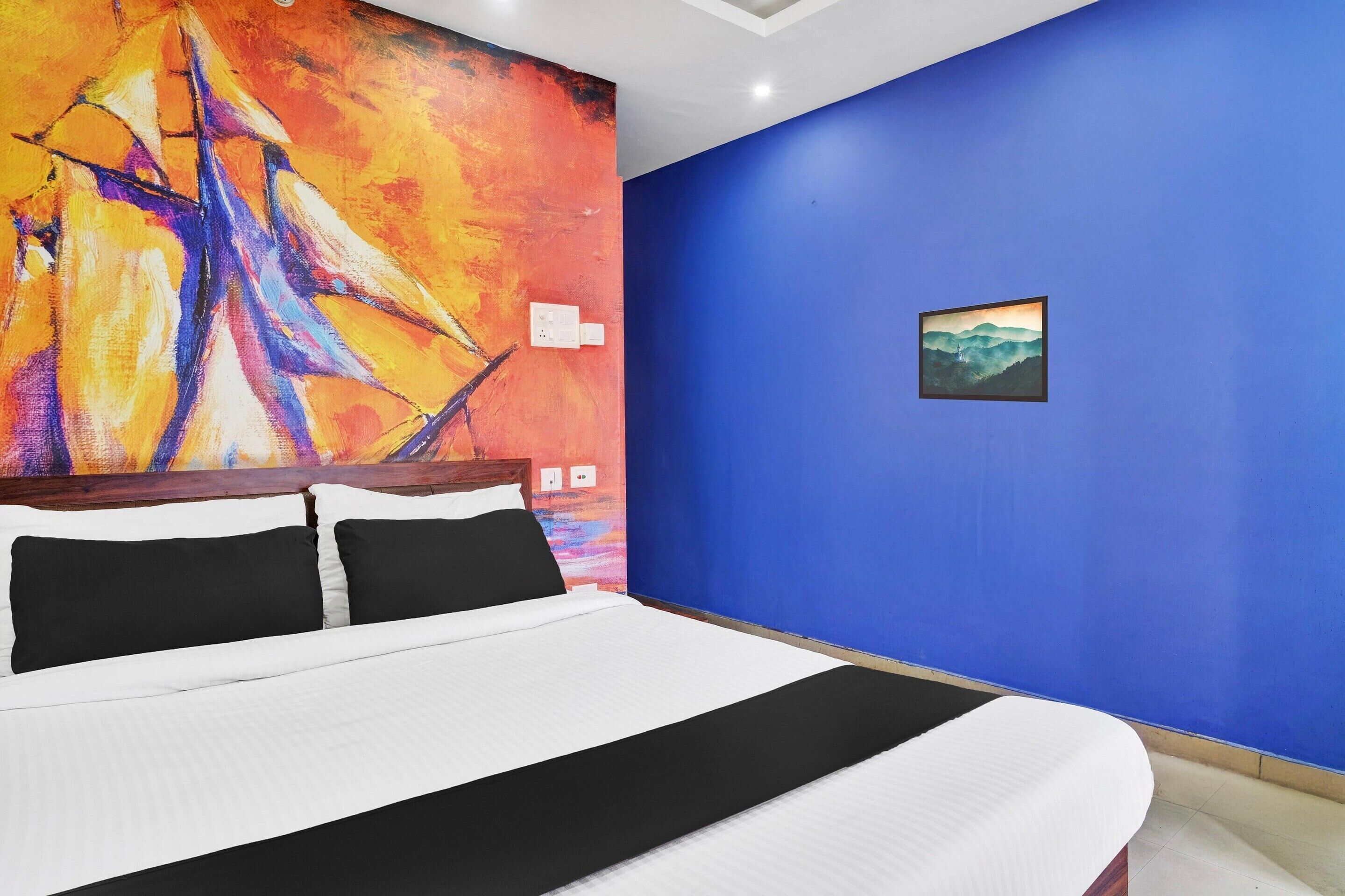 A bed with white and black bedding, a large abstract painting on the wall, and a framed picture on the blue wall.