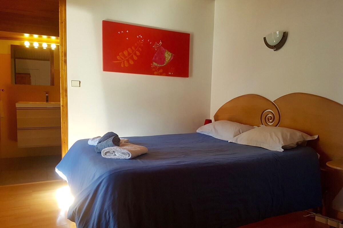 Een slaapkamer met een bed, een rode afbeelding, een nachtkastje en een houten hoofdbord.