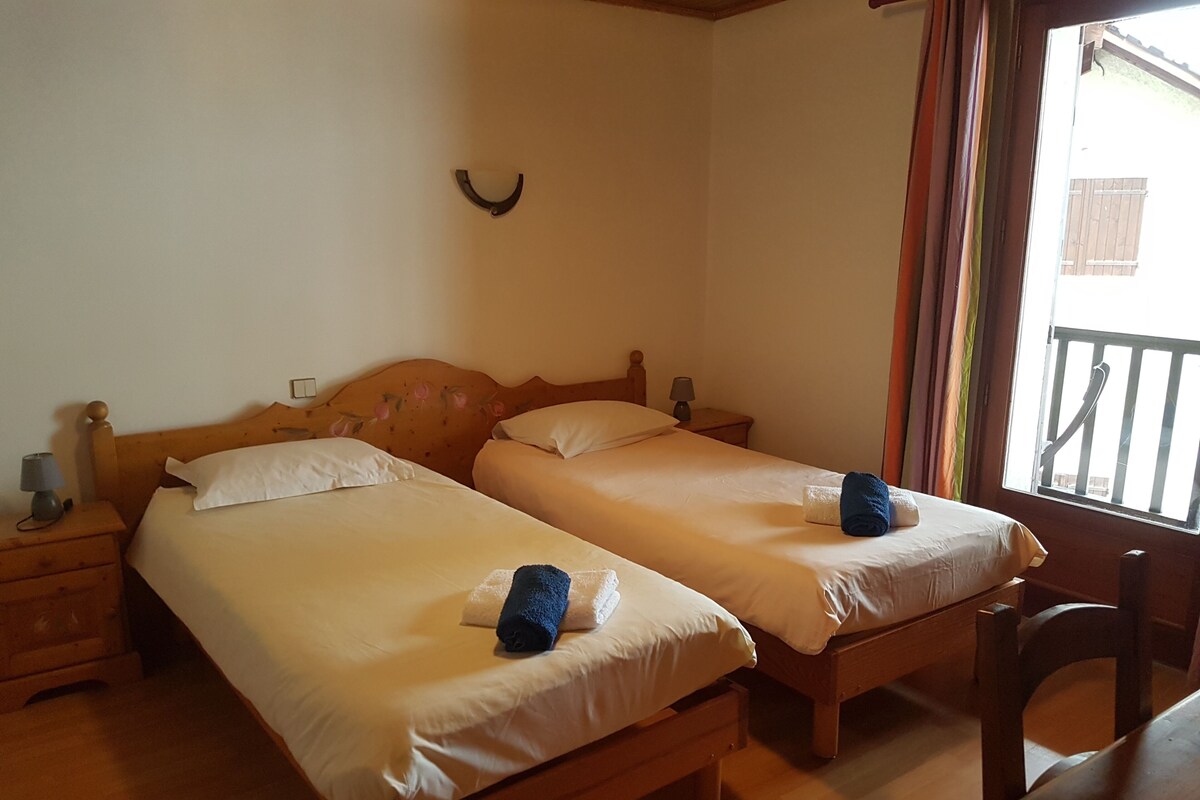Een kamer met twee houten bedden, een nachtkastje met een lamp en een raam met gordijnen.