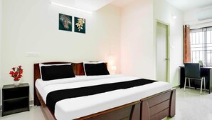 Hotellihuone, jossa on sänky, yöpöytä, työpöytä, tuoli ja taideteos seinällä.