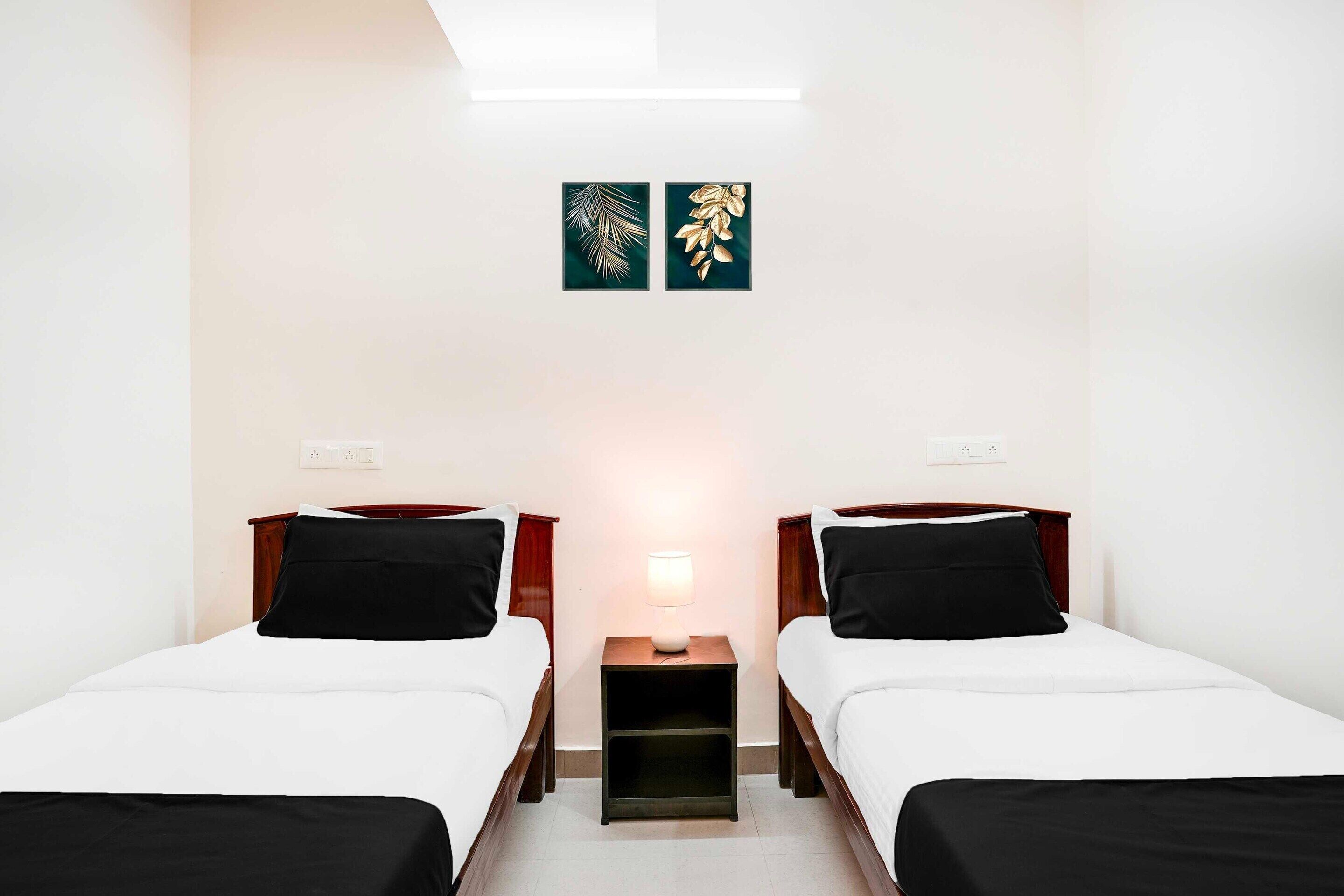 A hotel room with two single beds, a nightstand with a lamp, and two wall art pieces.