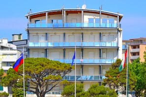 Un edificio de varios pisos con balcones, banderas y cielo despejado.