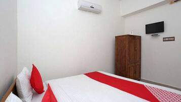 A bedroom with a bed, a wardrobe, a television, and an air conditioning unit.