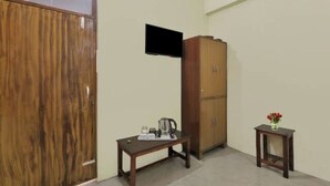 Una habitación con un armario de madera, una mesita con una tetera, un televisor montado en la pared y una pequeña mesa con un florero.
