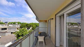 A balcony with a table and chairs, a glass door, and a view of buildings and trees. - Modern apartment near the beach (Lignano Sabbiadoro)