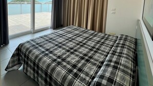Quarto de hotel com uma cama, uma janela grande e vista para o mar.