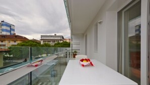 Ein Balkon mit weißem Tisch, Glasgeländer und Blick auf Gebäude.