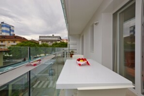 Ein Balkon mit weißem Tisch, Glasgeländer und Blick auf Gebäude.