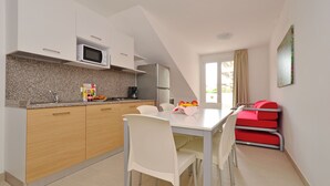 A modern kitchen with a microwave, refrigerator, and a dining area with a table and chairs. - Charming retreat just steps from the beach (Lignano Sabbiadoro)