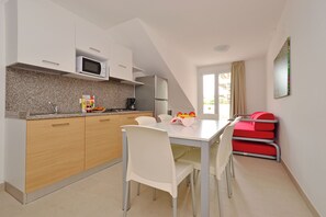 A modern kitchen with a microwave, refrigerator, and a dining area with a table and chairs. - Charming retreat just steps from the beach (Lignano Sabbiadoro)