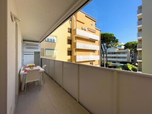 A balcony with a dining table and chairs, a small kitchen area, and a view of adjacent buildings. - Modern flat in a prime location (Lignano Sabbiadoro)