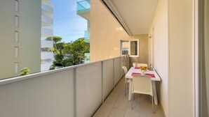 A narrow balcony with a white table and chairs, a small window, and a view of buildings and trees. - Modern flat in a prime location (Lignano Sabbiadoro)
