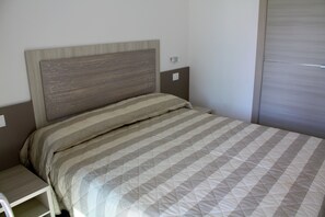 A neatly made bed with a striped bedspread and a headboard with a wood-like texture. - Lignano stay with parking (Lignano Sabbiadoro)