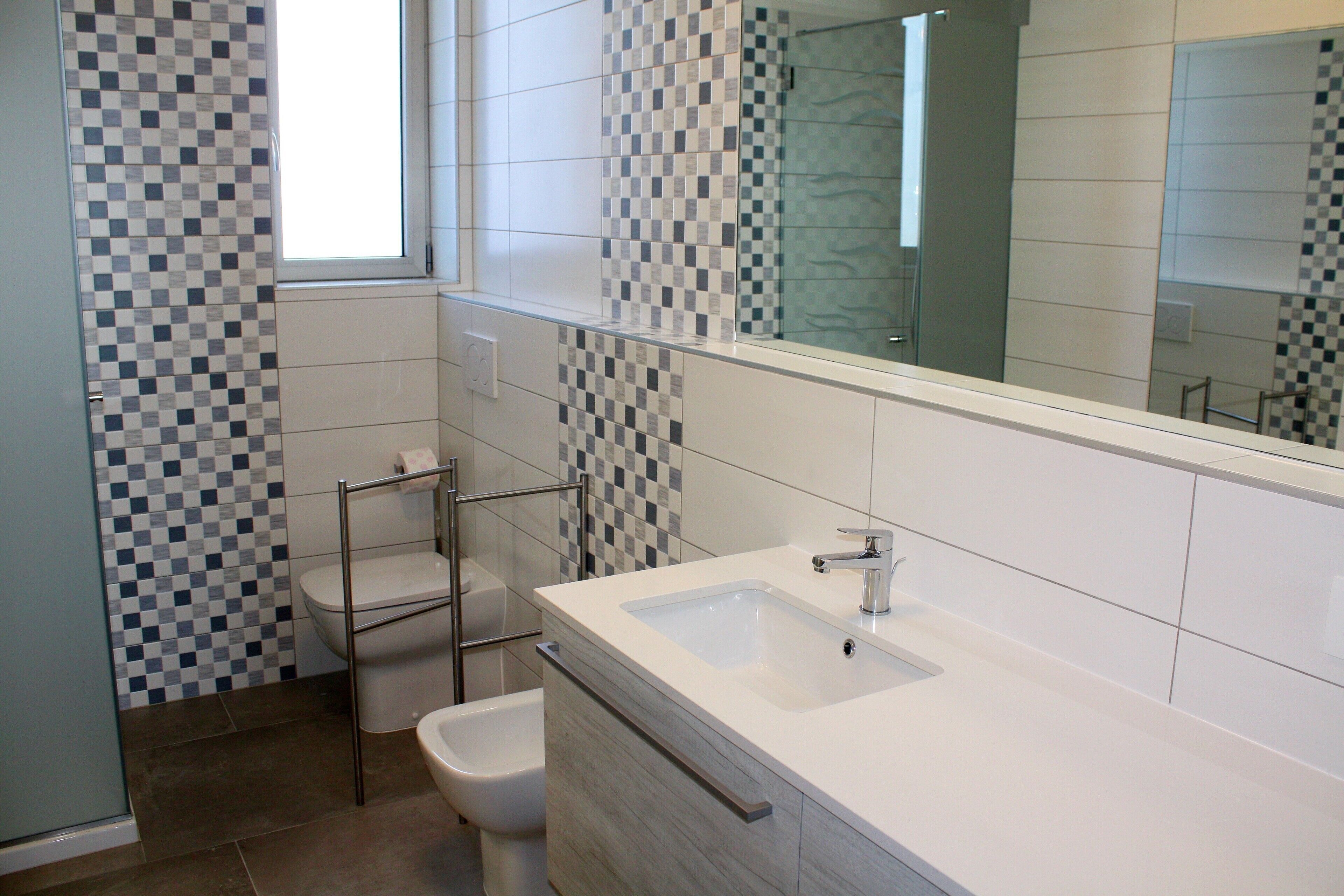 A modern bathroom with a checkered tile backsplash, a large mirror, and a white sink.