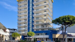 A multi-story building with balconies, a blue and yellow facade, and a clear sky. - Lignano apartment with parking (Lignano Sabbiadoro)
